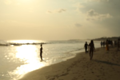 Photo of Blurred view of sandy beach with people walking near sea