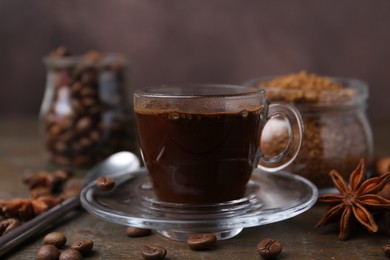 Photo of Cup of aromatic coffee, beans, instant powder and spices on wooden table, closeup