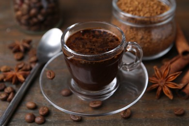 Photo of Cup of aromatic coffee, beans, instant powder and spices on wooden table, closeup