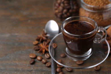 Photo of Cup of aromatic coffee, beans, instant powder and spices on wooden table, closeup. Space for text