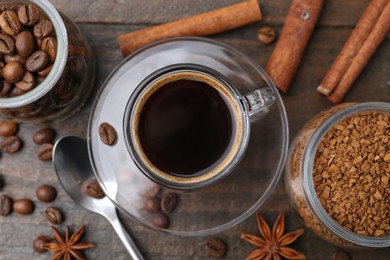 Photo of Cup of aromatic coffee, beans, instant powder and spices on wooden table, flat lay