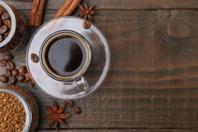Photo of Cup of aromatic coffee, beans, instant powder and spices on wooden table, flat lay. Space for text