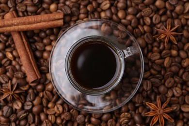 Photo of Cup with aromatic coffee, star anise and cinnamon on beans, top view
