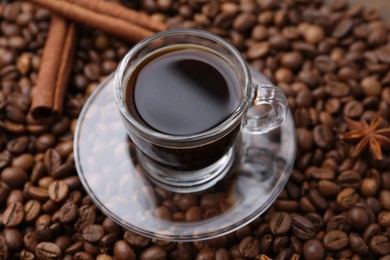 Photo of Cup with aromatic coffee, star anise and cinnamon on beans, closeup