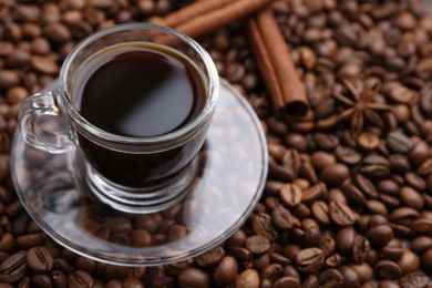 Photo of Cup with aromatic coffee, star anise and cinnamon on beans, closeup