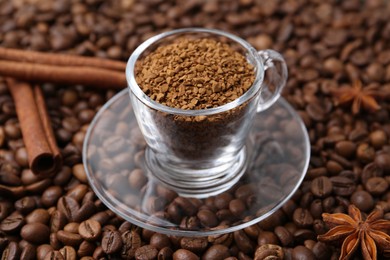 Photo of Cup with granulated instant coffee, star anise and cinnamon on beans, closeup