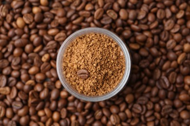 Photo of Glass jar with granulated instant coffee on beans, top view