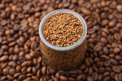 Photo of Glass jar with granulated instant coffee on beans, closeup