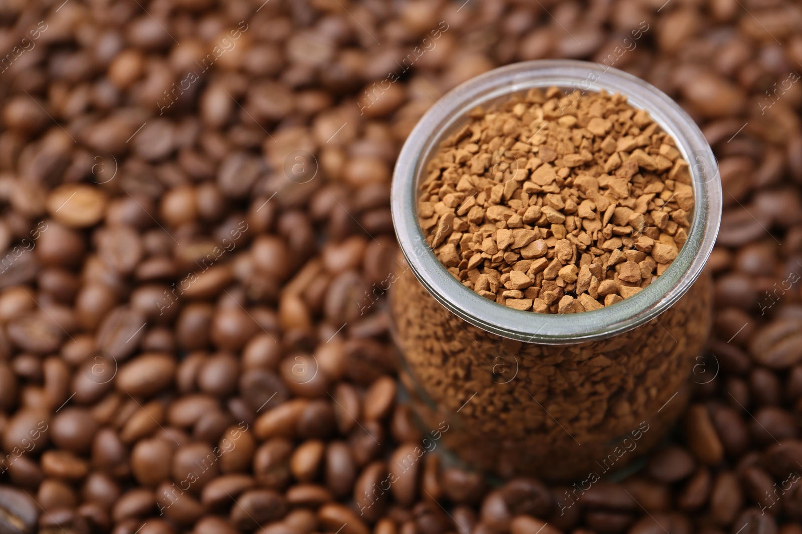 Glass jar with granulated instant coffee on beans, closeup. Space for text Photo of Glass jar with granulated instant coffee on beans, closeup. Space for text