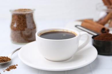 Photo of Cup of aromatic coffee and granulated instant coffee on white table, closeup
