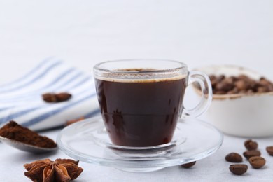 Photo of Cup of aromatic coffee, beans and star anise on white table, closeup