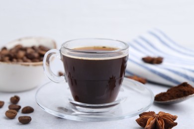 Photo of Cup of aromatic coffee, beans and star anise on white table, closeup