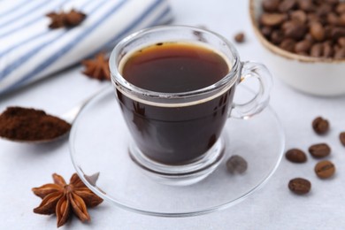 Photo of Cup of aromatic coffee, beans and star anise on white table, closeup