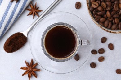 Photo of Cup of aromatic coffee, beans and star anise on white table, flat lay