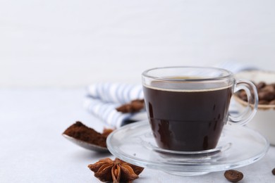 Photo of Cup of aromatic coffee, beans and star anise on white table, closeup. Space for text