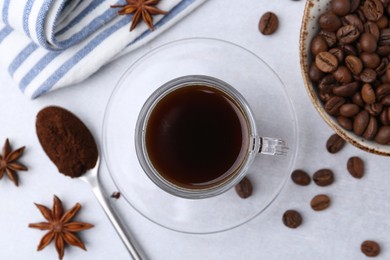 Photo of Cup of aromatic coffee, beans and star anise on white table, flat lay