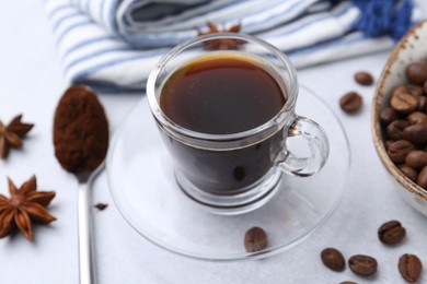 Photo of Cup of aromatic coffee, beans and star anise on white table, closeup