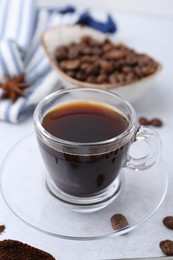 Photo of Cup of aromatic coffee, beans and star anise on white table, closeup