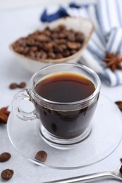 Photo of Cup of aromatic coffee, beans and star anise on white table, closeup