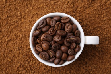 Photo of Cup of roasted beans on granulated instant coffee, top view