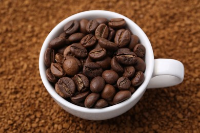 Photo of Cup of roasted beans on granulated instant coffee, above view