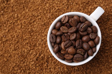 Photo of Cup of roasted beans on granulated instant coffee, top view. Space for text