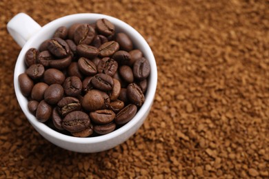 Photo of Cup of roasted beans on granulated instant coffee, closeup. Space for text