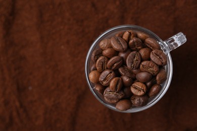 Photo of Cup of roasted coffee beans on powder, top view. Space for text