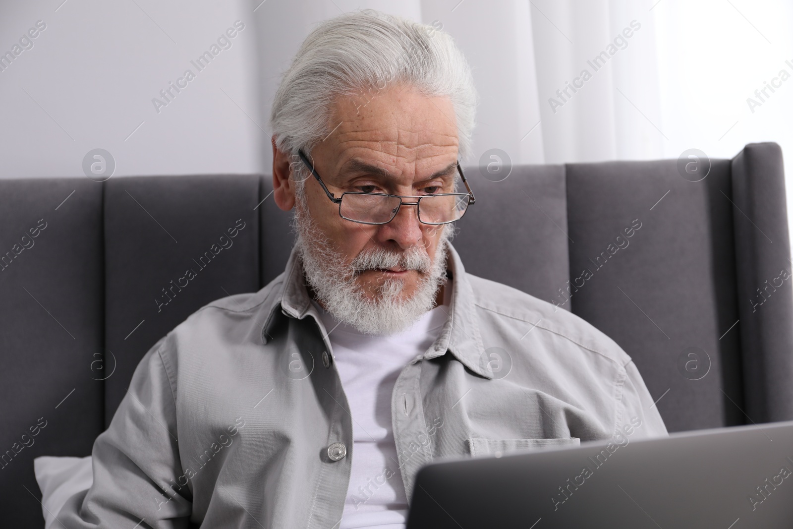 Senior man with vision problem using laptop on bed at home Photo of Senior man with vision problem using laptop on bed at home
