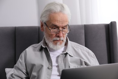 Photo of Senior man with vision problem using laptop on bed at home
