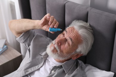Photo of Senior man applying eye drops on bed at home, above view