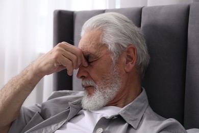 Photo of Senior man suffering from eyestrain on bed at home