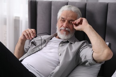 Photo of Senior man suffering from eyestrain on bed at home