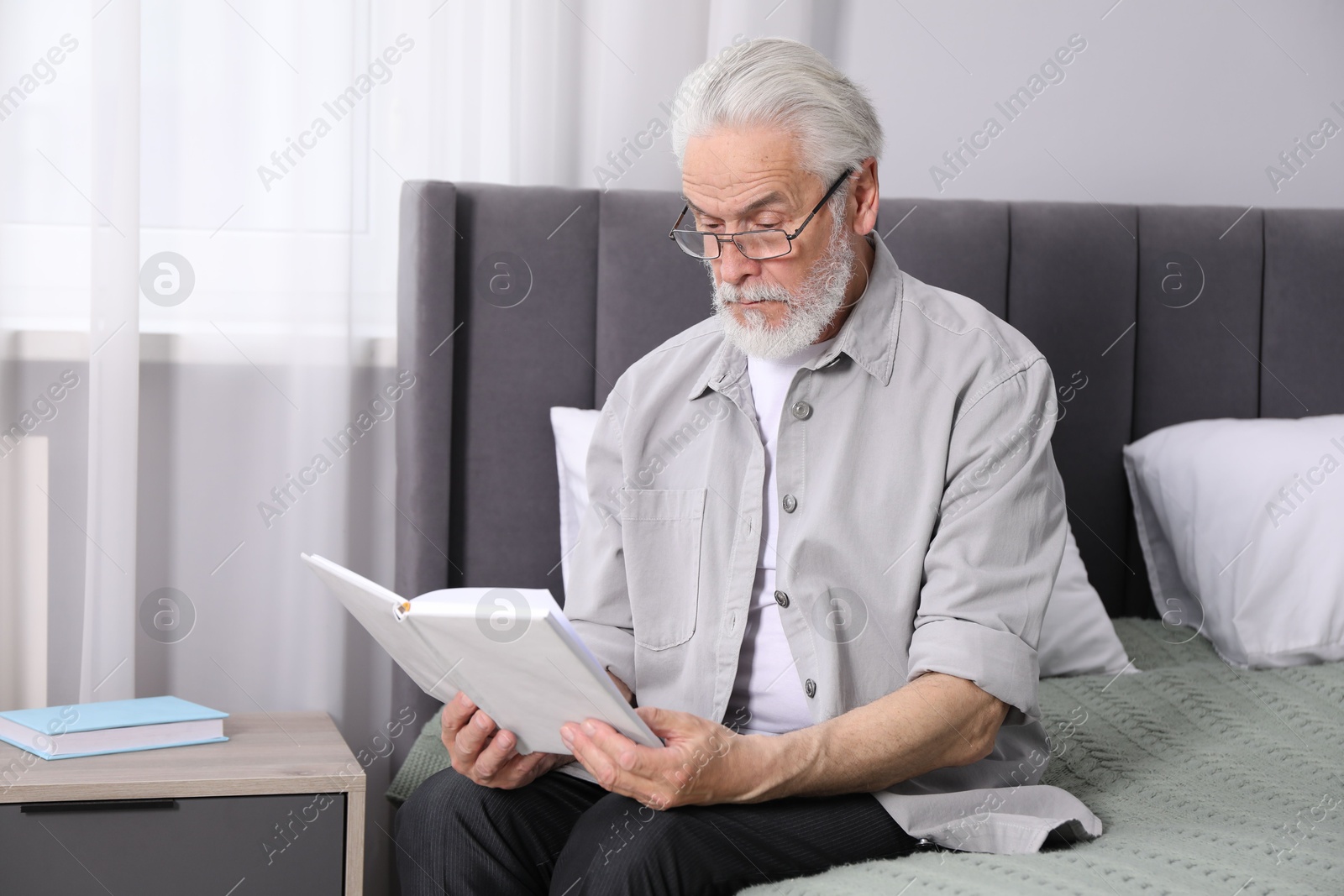Senior man with vision problem reading book on bed at home Photo of Senior man with vision problem reading book on bed at home