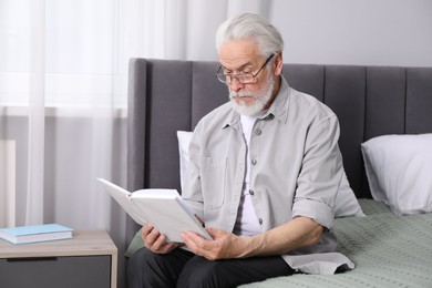 Photo of Senior man with vision problem reading book on bed at home