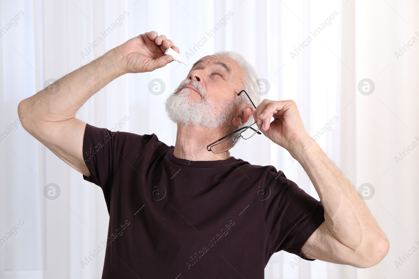 Senior man applying eye drops at home Photo of Senior man applying eye drops at home