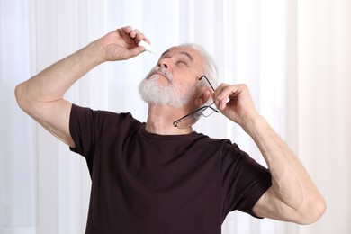 Photo of Senior man applying eye drops at home