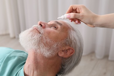 Photo of Woman dripping medication into man's eye at home, closeup