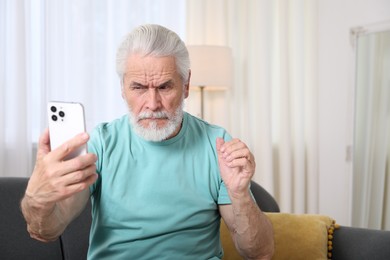 Photo of Senior man with vision problem using smartphone on sofa at home