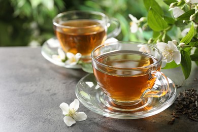 Photo of Aromatic jasmine tea in glass cups, brew and flowers on grey table outdoors, closeup. Space for text