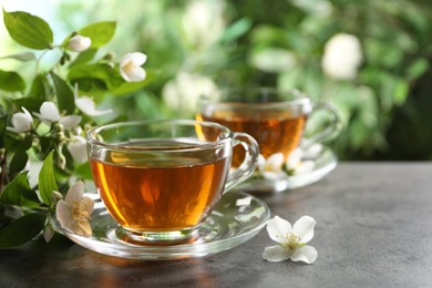 Photo of Aromatic jasmine tea in glass cups, flowers and green leaves on grey table outdoors, closeup. Space for text