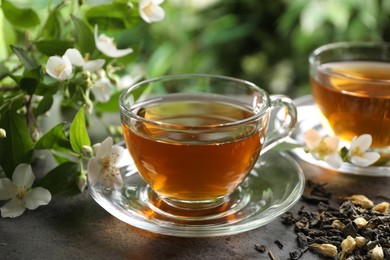 Photo of Aromatic jasmine tea in glass cups, brew and flowers on grey table outdoors, closeup