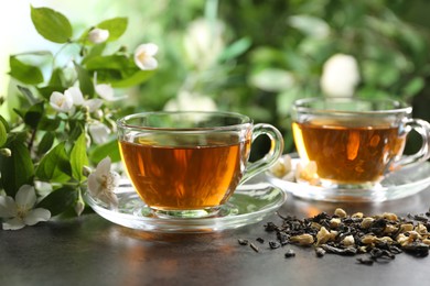 Photo of Aromatic jasmine tea in glass cups, brew and flowers on grey table outdoors, closeup