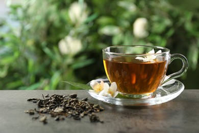 Photo of Aromatic jasmine tea in glass cup, brew and flowers on grey table outdoors, closeup