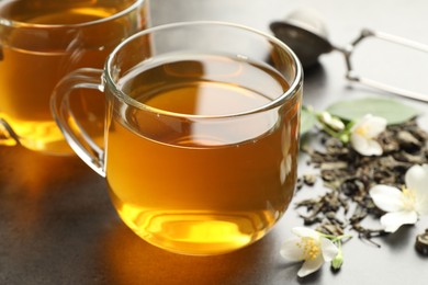 Photo of Aromatic jasmine tea in glass cups, brew and flowers on grey table, closeup