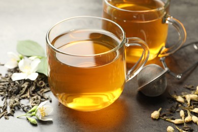 Photo of Aromatic jasmine tea in glass cups, brew and flowers on grey table, closeup