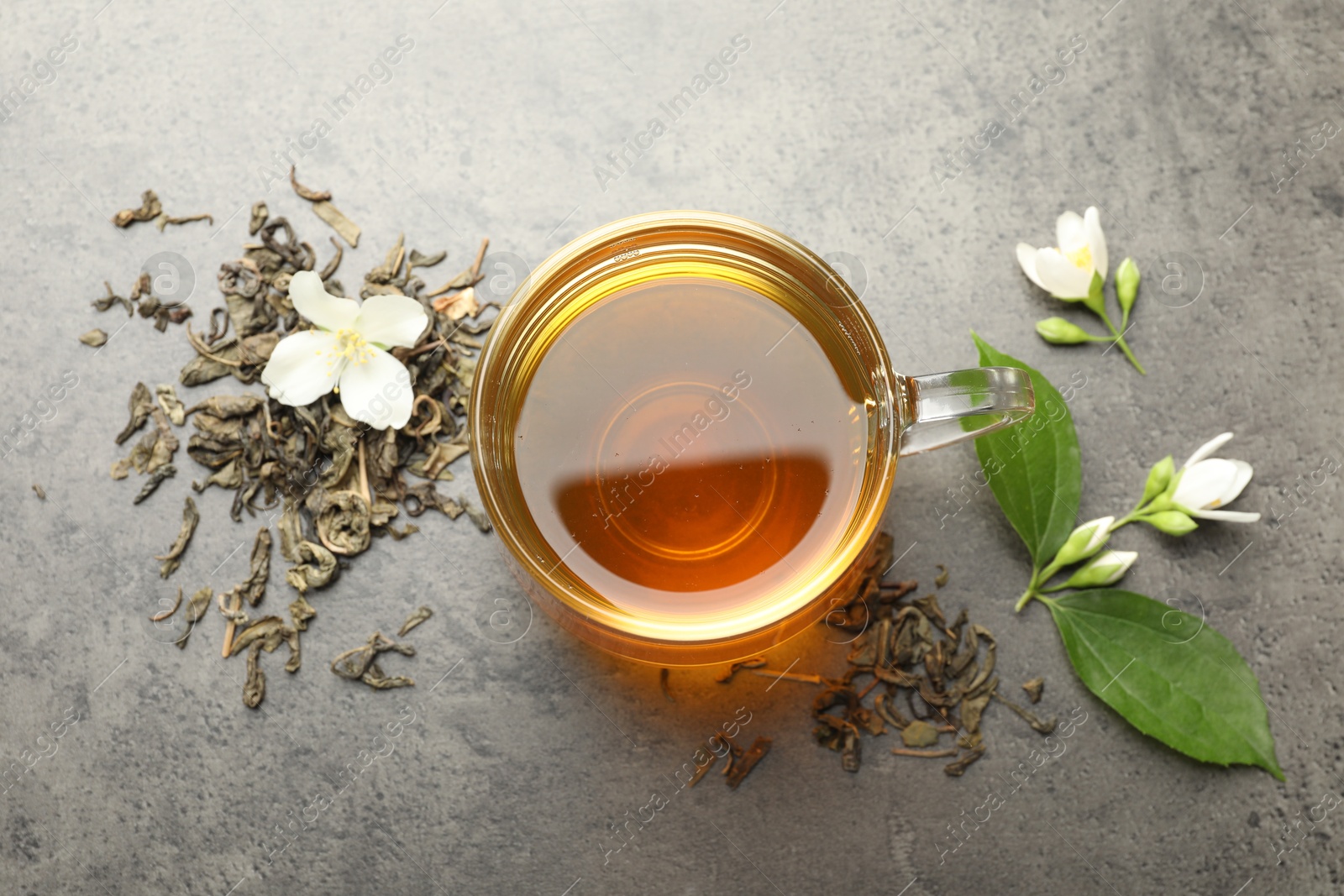 Aromatic jasmine tea in glass cup, brew and flowers on grey table, flat lay Photo of Aromatic jasmine tea in glass cup, brew and flowers on grey table, flat lay
