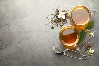Photo of Aromatic jasmine tea in glass cups, brew and flowers on grey table, flat lay. Space for text