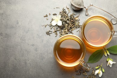 Photo of Aromatic jasmine tea in glass cups, brew and flowers on grey table, flat lay. Space for text