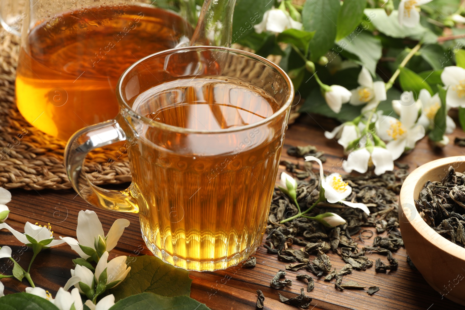 Aromatic jasmine tea in glass cup, teapot, brew and flowers on wooden table, closeup Photo of Aromatic jasmine tea in glass cup, teapot, brew and flowers on wooden table, closeup